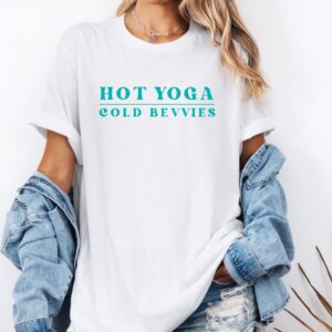 Female yogi with long hair wearing a white funny yoga t-shirt with a saying that says hot yoga cold bevvies.