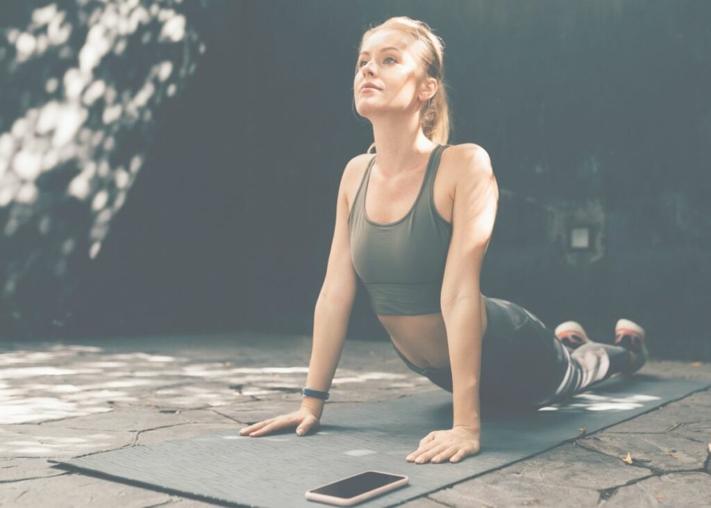 Female yogi practicing yoga outside on a yoga mat using a yoga app. Make.