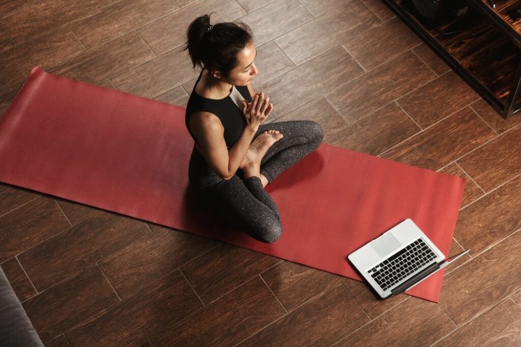 Female yogi sitting in half lotus pose on her yoga mat taking an online yoga teacher training class. Make.